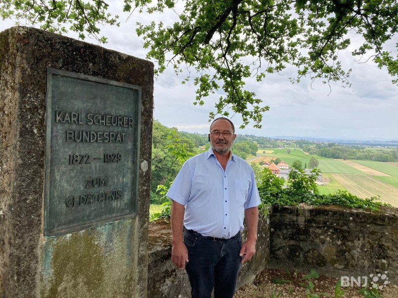 Eric Dietrich, le maire de Gampelen, qui pose à côté de la plaque érigée en l'honneur de Karl Scheurer, ancien conseiller fédéral qui a vécu dans le village.