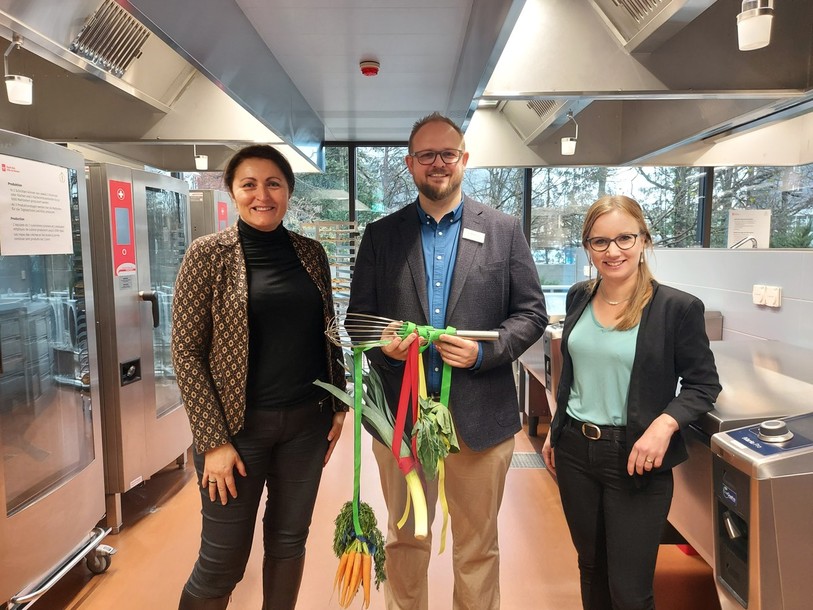 Glenda Gonzalez Bassi ( à gauche) et Léna Frank (directrice des travaux publics, à droite) ont remis un fouet symbolique de bienvenue à Gunnar Krening, le responsable de la cuisine.