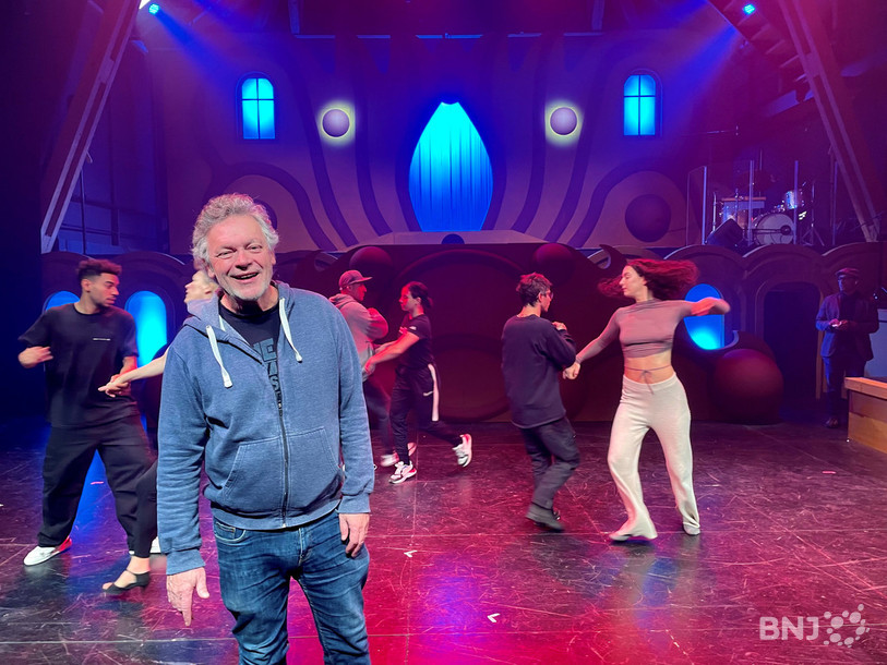 Le metteur en scène Gérard William pose sur scène tandis que les danseurs et danseuses de La Décharge s’entraînent.

