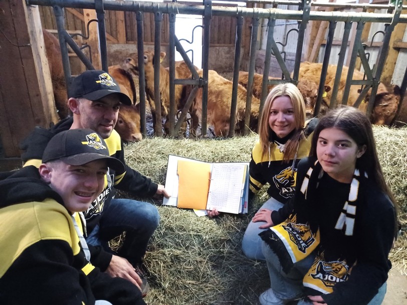 La famille Hulmann (Noé, Julien, France et Lara) pose devant un box de veaux portant le nom de joueurs du HC Ajoie. Les parents tiennent le classeur des naissances 2023.