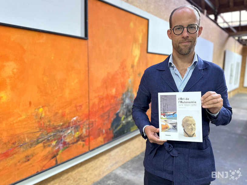 Le commissaire de l’exposition « L’art de l’autonomie » Yves Guignard pose avec son catalogue devant l’œuvre « Triptyque du soleil » de l’artiste jurassien Jean-François Comment.