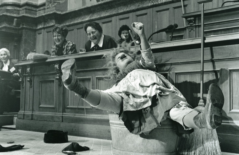 Gardi Hutter dans un numéro de femme de ménage et de bouffonne dans la salle du Conseil national à l’occasion du 700e anniversaire de la Confédération - Session des femmes, février 1991. / Photo : Lisa Schäublin, Berner Zeitung (StAB PBA BZ D 102)