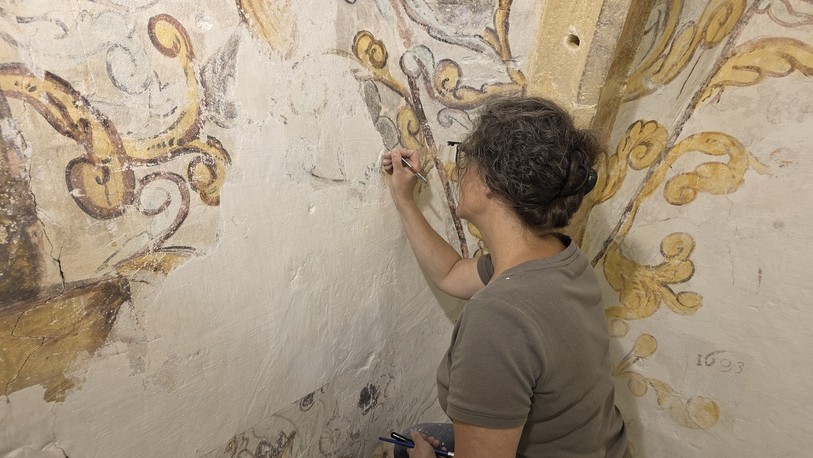 Isabelle Capt Gigon gratte la peinture blanche avec patience pour révéler le trésor caché.