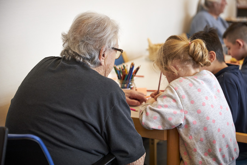 Photo d'une dame âgée réalisant un coloriage avec des enfants