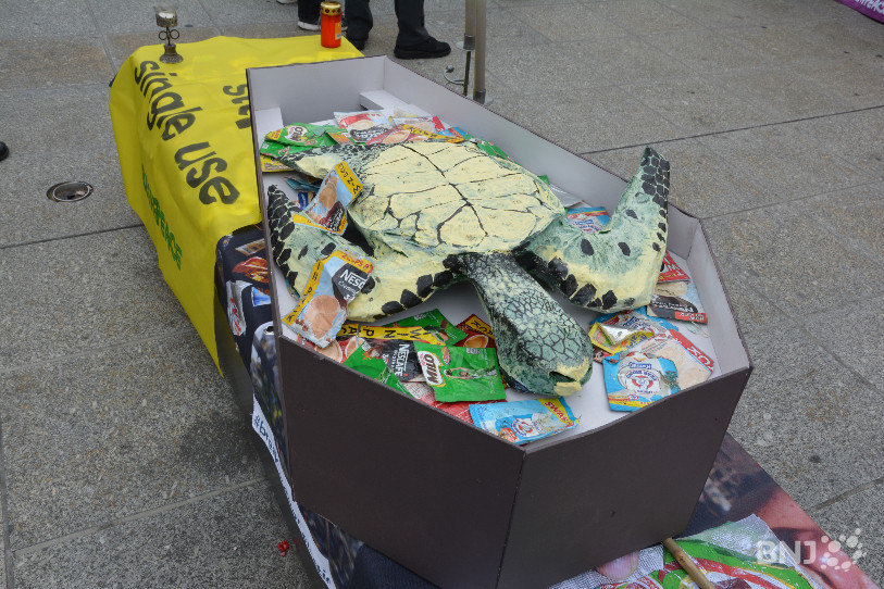 Pour sensibiliser le public à la pollution plastique, une tortue en papier mâché dans un cercueil rempli d'emballages.