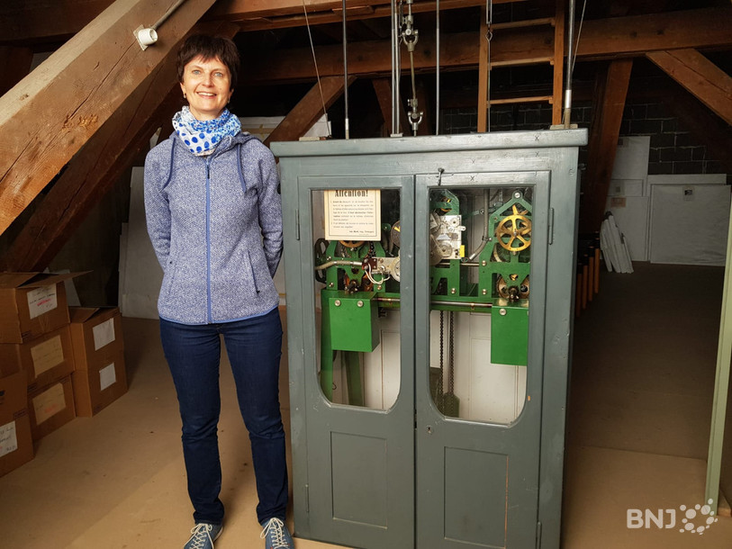La directrice de la Bibliothèque de la Ville, Sylvie Béguelin, pose à côté du mécanisme de la grande horloge de la bibliothèque.