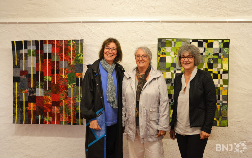 Trois membres de l’Association jurassienne - Marie-Thérèse Terazzi, Marie-Claire Luzieux et Maria Vuilleumier (de gauche à droite) – posent devant des œuvres exposées à la galerie Le Caveau.