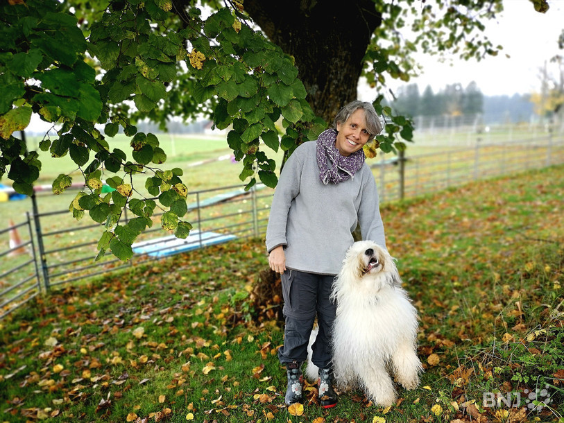 Danièle Lachat et Michka, jeune Bobtail d'une année et demi, posent devant le parcours d'agility, devant la ferme.