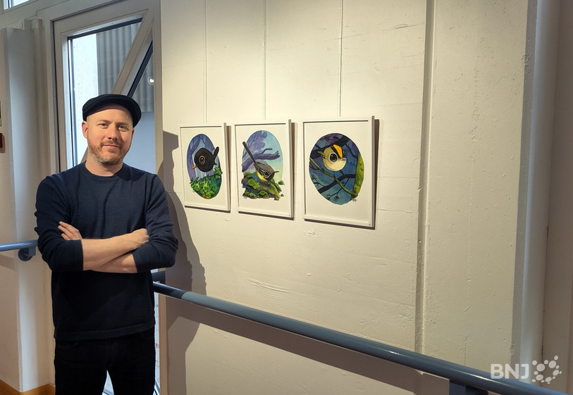 Guznag prend la pose devant quelques-uns des dessins d'oiseaux qu'il expose dans la galerie des Planchettes à Porrentruy.