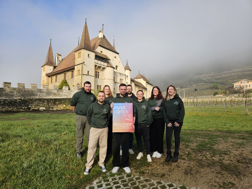 Une partie des membres de l’association MusicÔvignes posent fièrement avec l’affiche de la troisième édition du festival devant le Château de Cressier.