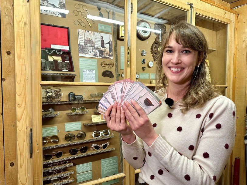 La conservatrice du Musée de la vie jurassienne Nathalie Zürcher pose avec le jeu de cartes « Patrimoine en jeu » devant la nouvelle vitrine de l'exposition dédiée à l'optique.