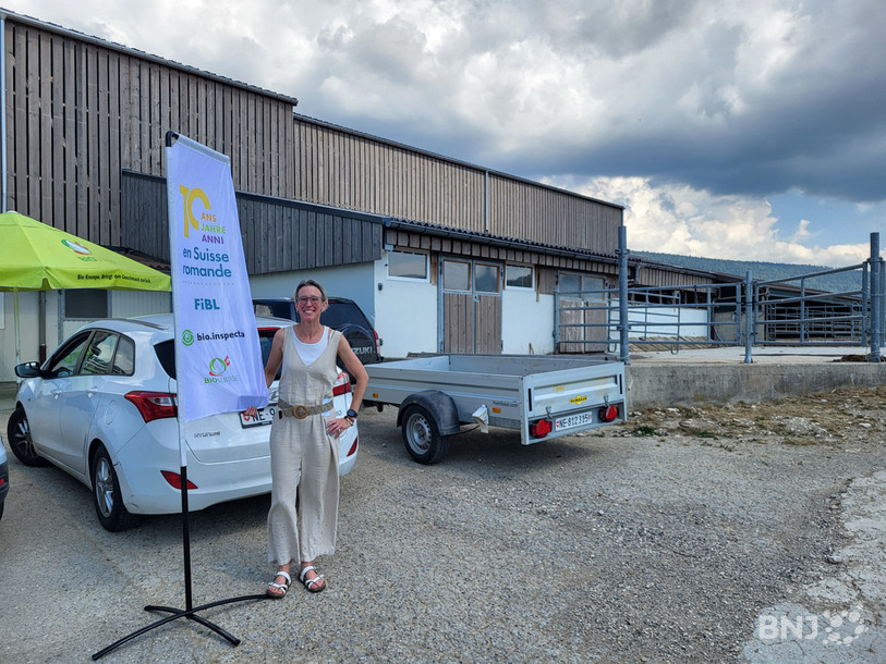 Claire Berbain, chargée de communication pour le FiBL, devant le drapeau d’anniversaire érigé devant le domaine de la famille Challandes.