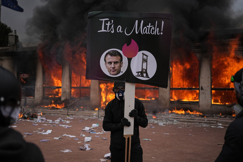 Un manifestant tient une pancarte arborant une photo du président français Emmanuel Macron devant un office de tourisme en feu à Lyon. (Photo : AP/Laurent Cipriani)