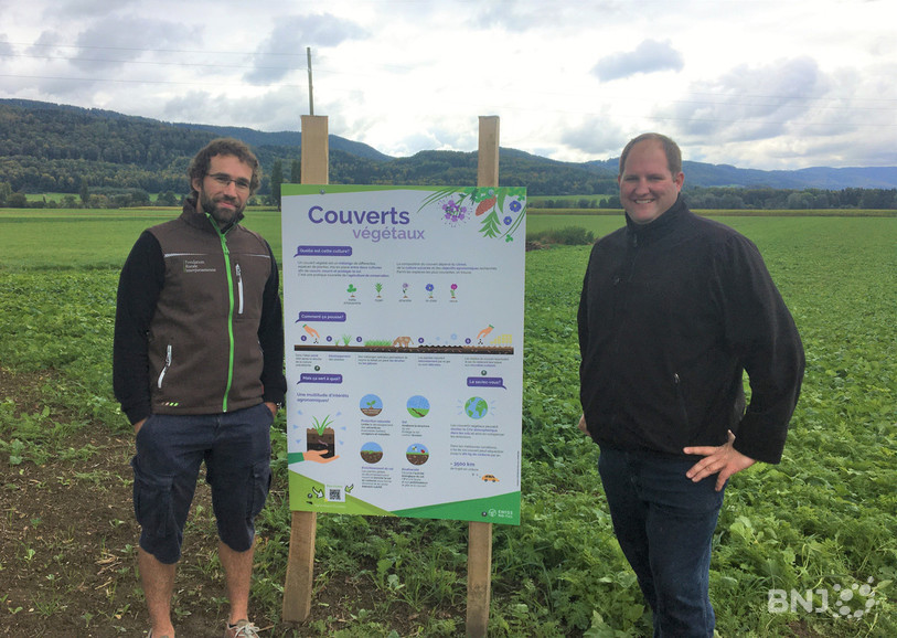 Luc Scherrer, conseiller à la Fondation rurale interjurassienne, et Fabrice Nagel, agriculteur, pose à côté d'une affiche donnant des informations sur les couverts végétaux.