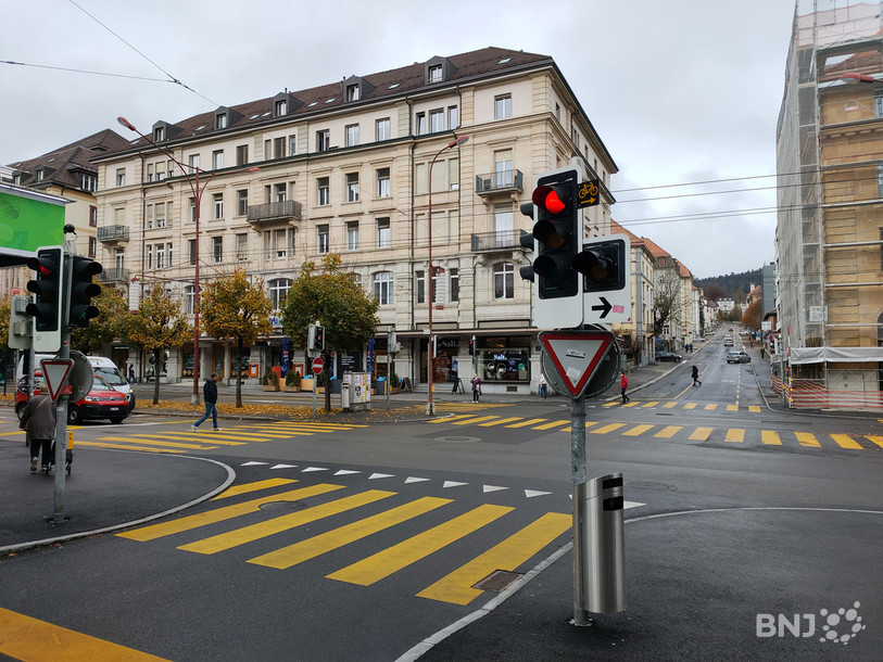 Une plaquette avec un vélo jaune est fixée à côté du feu rouge: à ce carrefour de La Chaux-de-Fonds, les cyclistes ont le droit de tourner à droite au feu rouge, tout en cédant le passage aux piétons et aux voitures.