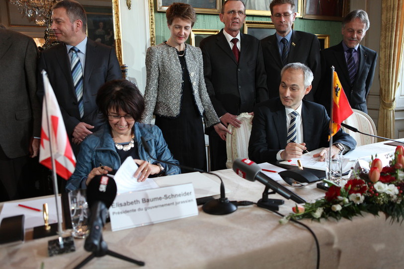 Elisabeth Baume-Schneider signe la déclaration d'intention sous les yeux de Bernhard Pulver et de Simonetta Sommaruga, encadrés par des conseillers d'Etat et du vice-chancelier du canton de Berne