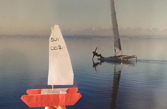 Un catamaran en papier réalisé par Solène, avec en fond son frère Robin sur son catamaran