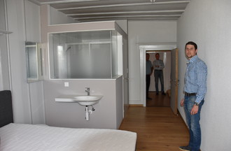 Une chambre type avec en arrière plan la salle de bain. Elle a été construite de manière à préserver la construction d'origine, notamment le plafond.